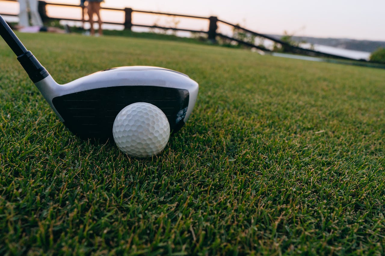 A close-up image of a golf ball and club on lush grass during sunset.