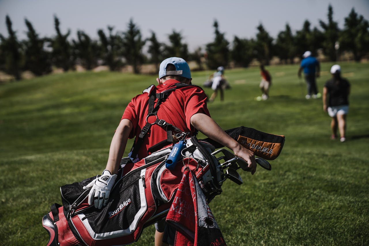 A golfer in red carrying a bag on a lush green golf course during a sunny day.