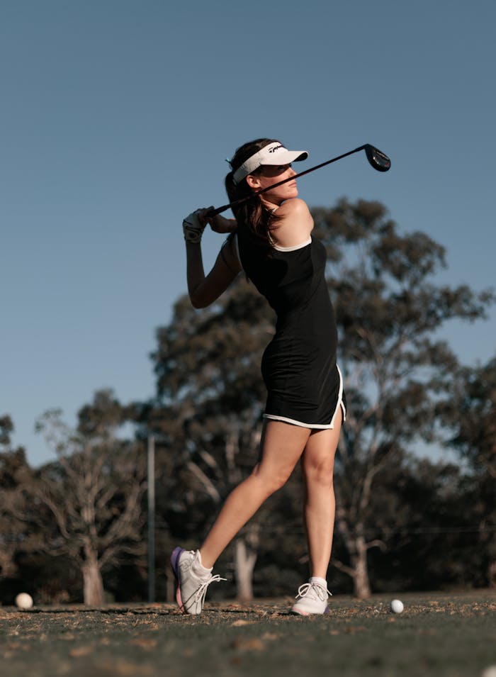 A woman golfer swings her club on a sunny day in an open field, showcasing perfect form.
